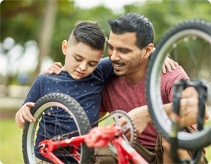 A father and son inspect the tire of a small bicycle.